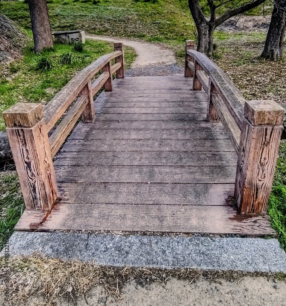 Obraz premium traditional wooden bridge over a stream in a park with a path