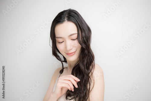 白背景に綺麗な黒髪をなびかせるロングヘアでパーマの女性　ヘアケアやトリートメントイメージ目を閉じる