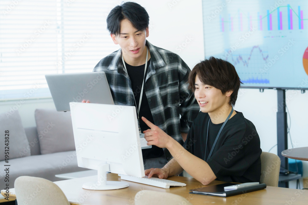 Obraz premium オフィスでパソコン作業をするカジュアルな服装の若い日本人男性2人