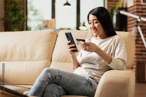Foto Remote asian manager happily using cellphone and debit card for mobile banking