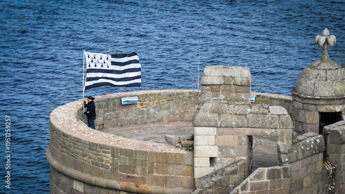 Aerial view of a Bretagne flag waving strongly from a stone tower of Chateau du Taureau overlooking the deep blue sea, Plouezoc'h, Bretagne, France.