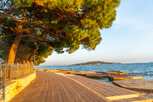 Obraz na plátne Coastal promenade with pine trees and sea view during sunset, featuring a clean pedestrian path