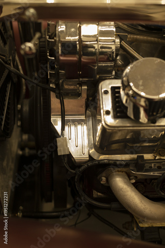 Polished chrome engine components with belt and hoses, aluminum block and ignition elements, tactile grease and oil textures under warm workshop light