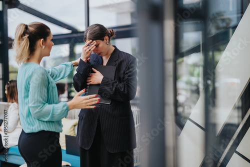 Fotografie A distressed businesswoman is comforted by a female coworker while holding a folder