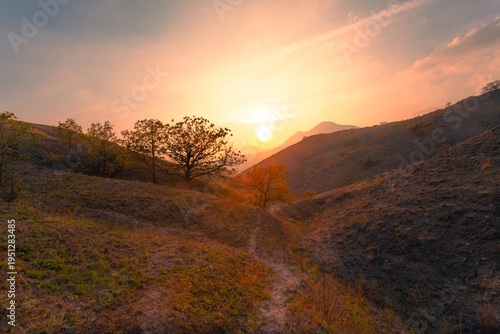 A gorgeous sunset scene with a pathway between mountain hills under a painted sky with clouds.