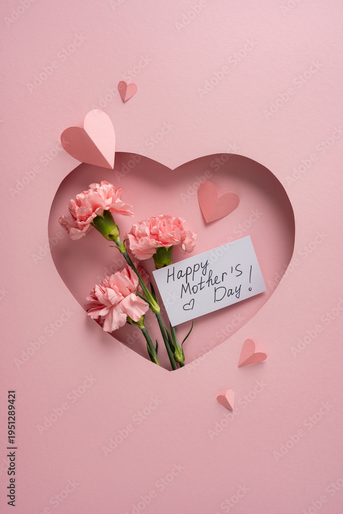 Obraz premium Happy Mother's Day vertical greeting card with pink carnations tucked into a heart-shaped paper cutout, handwritten note paper hearts conveying love, gratitude and a soft pastel feminine celebration
