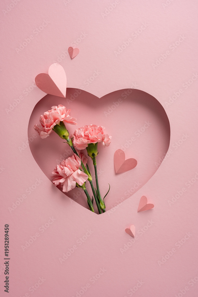 Fototapeta premium Soft pink vertical carnations arranged in a heart-shaped paper cutout with small paper hearts, evoking love and appreciation for Happy Mother's Day celebrations and handmade greeting concepts