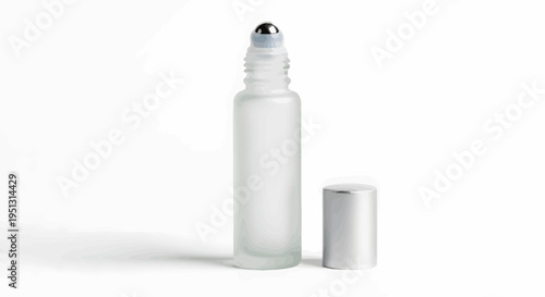 A clear glass perfume bottle with a silver cap sits on a white surface next to its open cap.