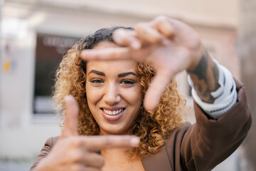 Smiling woman with curly hair framing face with hands in urban setting
