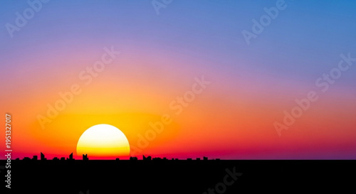 Vibrant sunset with orange yellow and blue hues over silhouette of trees and landscape at dusk
