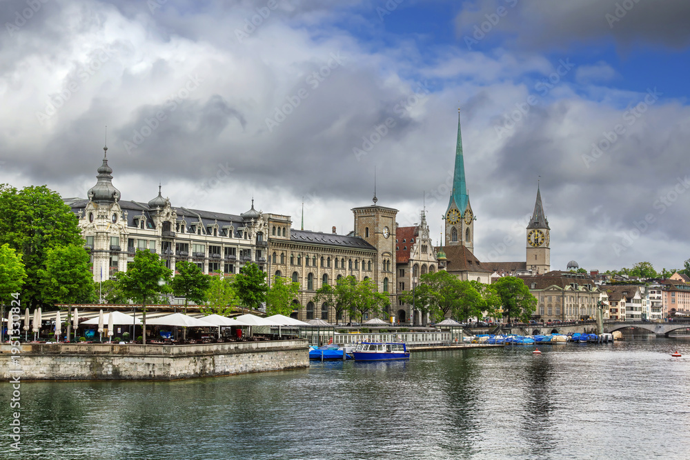 Fototapeta premium Fraumunster and St. Peter churches on the Limmat river bank in Zurich, Switzerland. Historic city buildings and cloudy June sky.