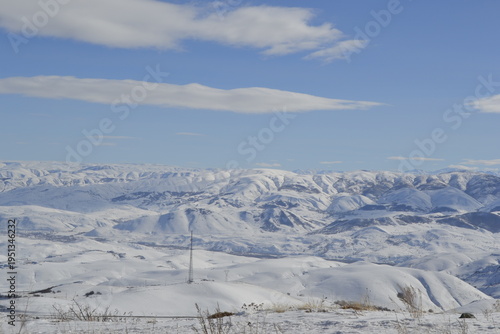 a vast mountain range under a soft blue sky with long white clouds the rolling snow-covered hills
