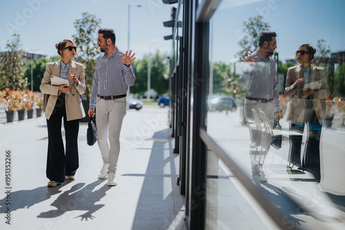 Fotografie Two business colleagues walk and talk while carrying folders outside a modern office