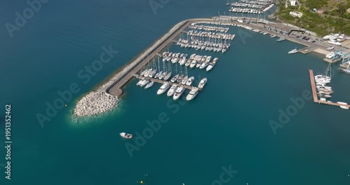 Aerial view of a single, small white boat with a simple cabin navigates the narrow mouth of a stone-built breakwater.