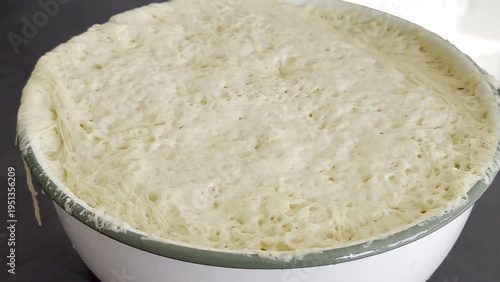 Dough rising in a large white bowl on a dark countertop, showing the progression of fermentation with bubbles forming and surface expanding over time