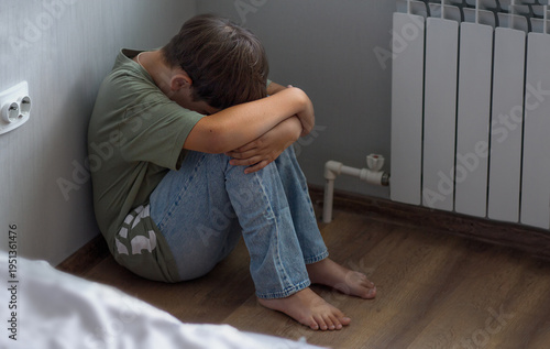 an offended child sits in the corner of the room. the boy hides his head in his knees, closing himself off from problems.