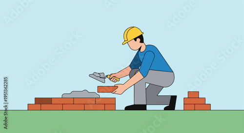 A person wearing a hard hat lays bricks with a trowel on a grassy area