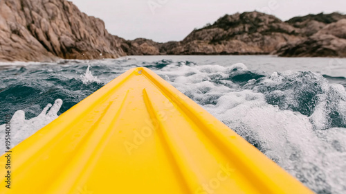 A yellow kayak rides a wave between mountain shores.