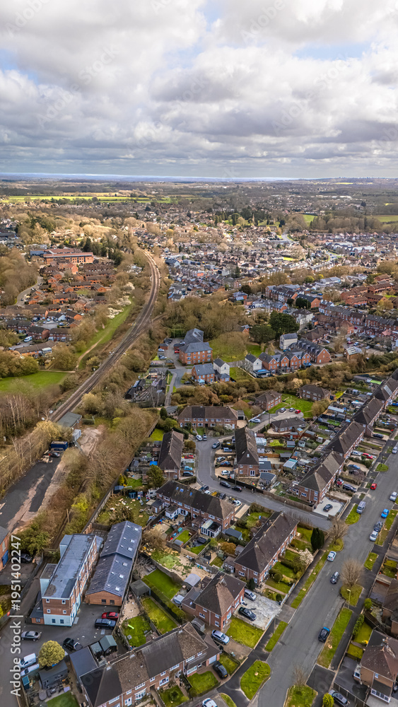 Obraz premium Portrait aerial drone shot overlooking Romsey, Hampshire with residential housing and railway track around quiet roads on overcast sunny spring day