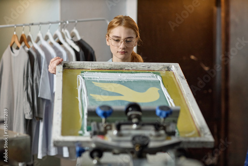 Foto Caucasian young adult woman screen printing bird design onto fabric, standing in