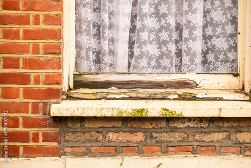 Rotten peeling wooden window frame on red brick house exterior