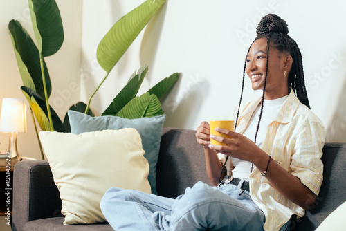 Happy woman is relaxing on comfortable couch at home, enjoying warm drink