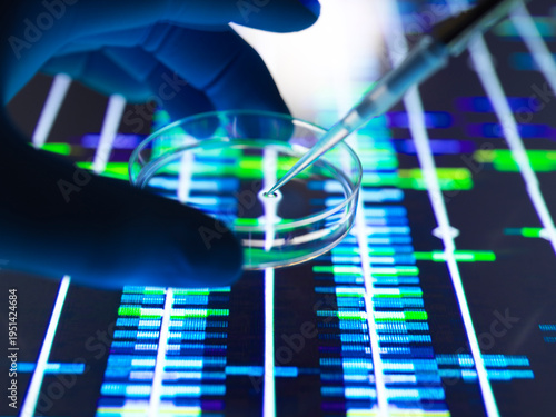 A gloved hand holds a petri dish above a DNA sequencing analysis display.