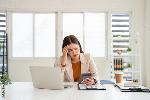 Young stressed businesswoman faces financial problem holding calculator and touching her head.