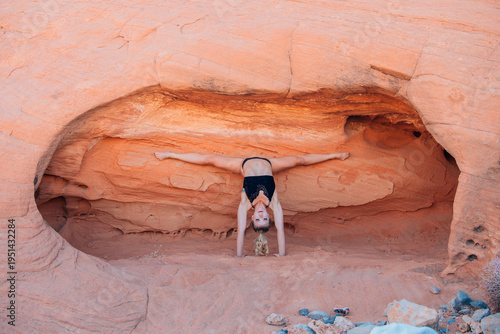 Woman doing a handstand in a rocky alcove with orange sand and rock formations. WA, USA