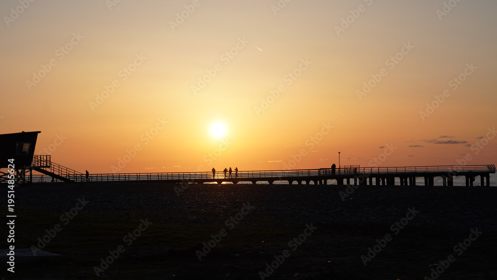 Obraz premium Silhouetted figures on pier at sunset with lifeguard tower in background