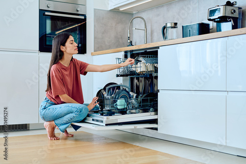 Canvastavla Woman loading dirty dishes into an open dishwasher in a bright, contemporary res