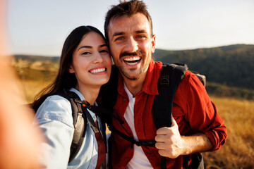 Couple having fun taking selfies while hiking in nature on sunny summer day