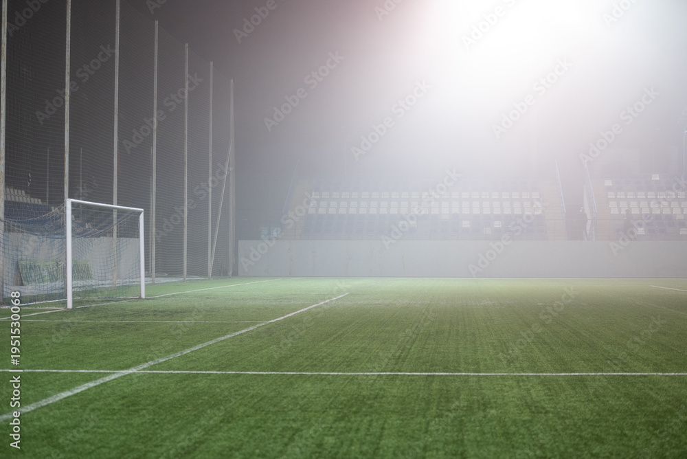 Fototapeta premium Foggy indoor soccer field with goalpost and empty spectator seating