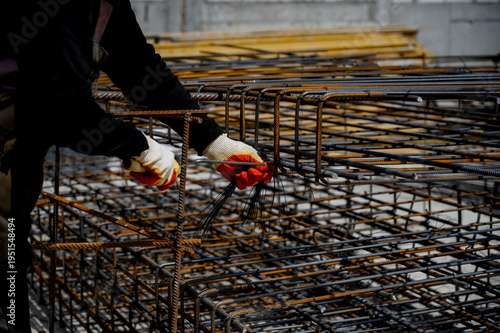Foto Worker assembling steel rebar framework at construction site indoors