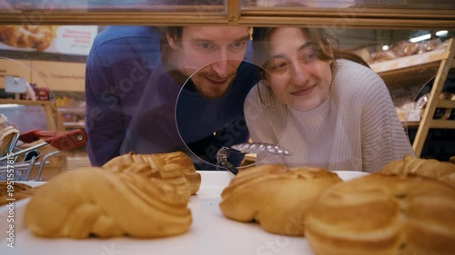Happy young man and woman choosing fresh buns and putting them in a bag at the grocery store