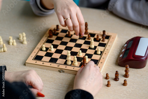 Hands of players move chess pieces on wooden board during game