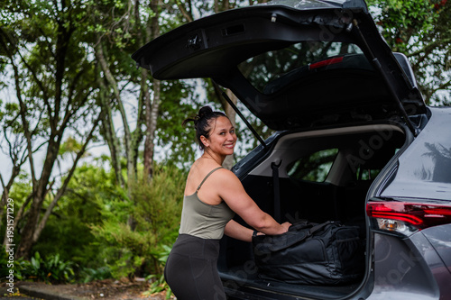Mixed race woman unloading sports bag from open car boot at parking area