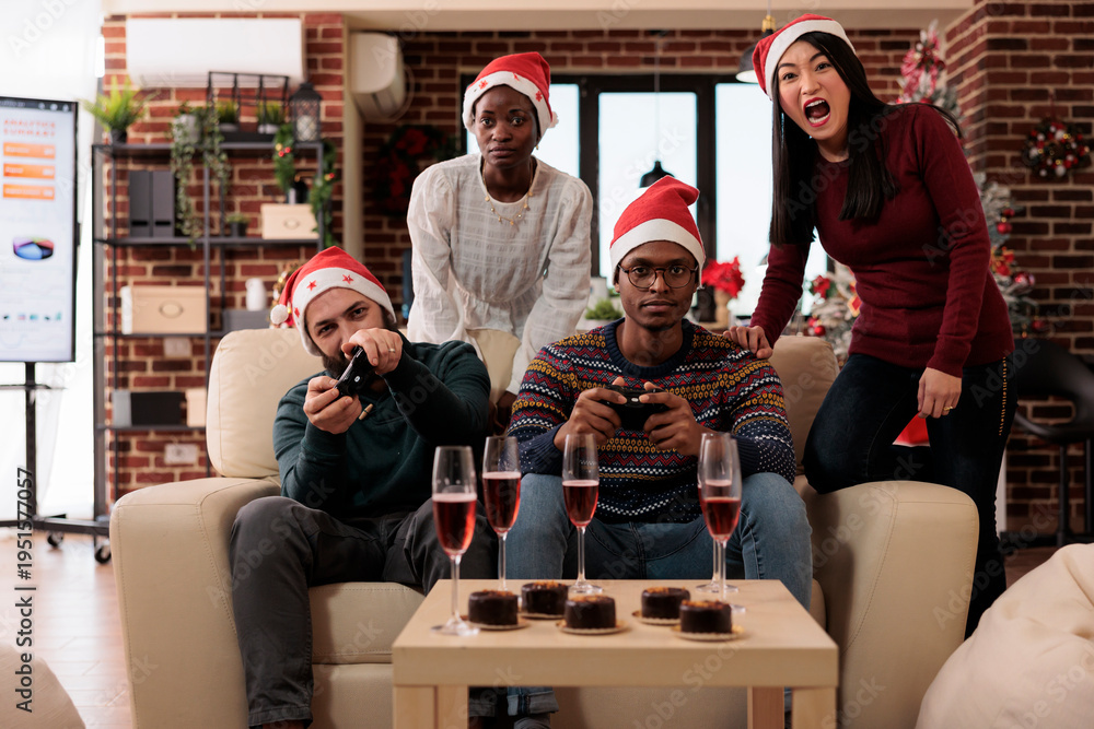 Obraz premium Festive coworkers playing online video games to celebrate christmas eve at office party with holiday decorations. People enjoying gaming competition during xmas winter festivity.