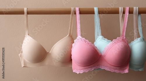Four bras hang neatly on a wooden rod. Colors range from beige to pink and light blue. Each bra has unique lace or texture details. Image perfect for fashion, retail, or lingerie-themed content