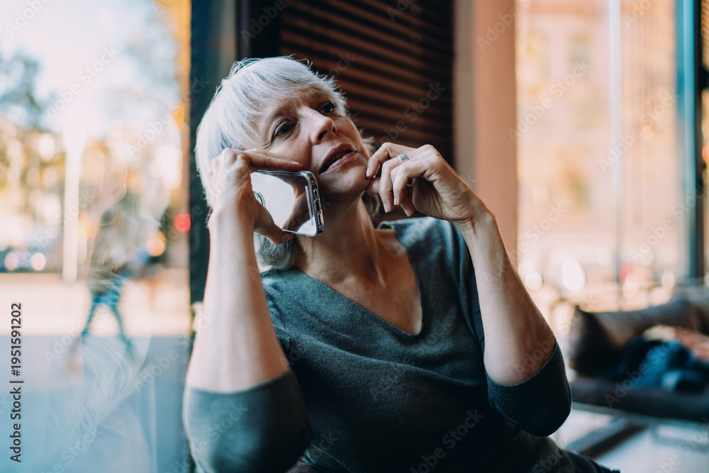 Fototapeta premium Elegant senior woman listening with smartphone held to ear, reflecting concentration and thoughtful conversation in digital communication. Realistic tech moment.