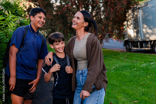 Two Maori boys and a woman share laughter while standing on a pathway in a suburban area in New Zealand