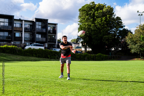Maori man throwing a rugby ball on a green field at a local park