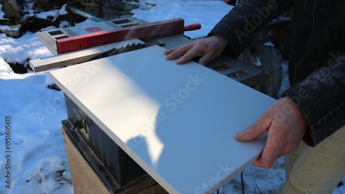 In an open woodworking shop, a carpenter presses a compressed board against the work surface of a circular saw to cut the workpiece, using an end saw to process building materials