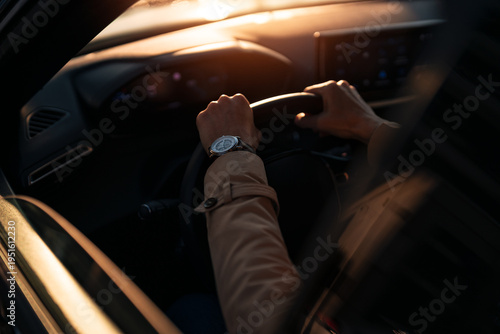 Driver hands on steering wheel with wristwatch at sunset