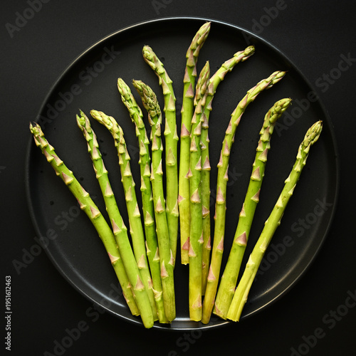 Fresh asparagus spears arranged on black plate, top view minimal composition for healthy organic food concept.