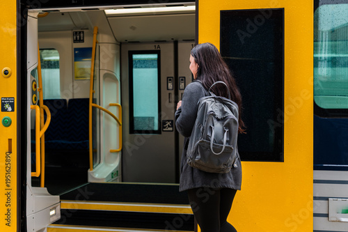 A woman entering a train at the station while holding a backpack on a rainy day in New Zealand