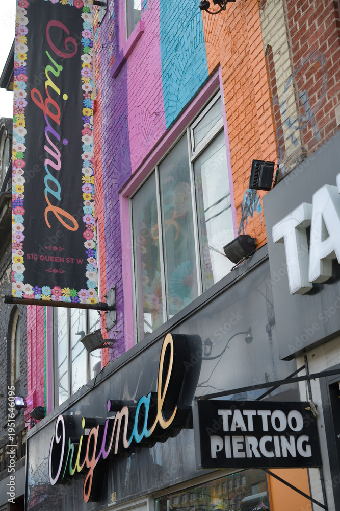 Fototapeta premium projecting Tattoo/Piercing sign and exterior building signs of Original, a women's clothing store, 515 Queen St W, Toronto