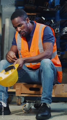 African American worker feeling overwhelmed and tired, taking a break from extreme job stress and burnout in an industrial storage warehouse.