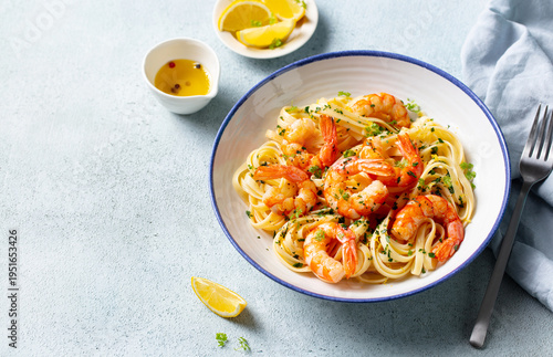 Fettuccine with succulent shrimp, enhanced with lemon slices, fresh parsley, and a drizzle of olive oil. Blue-grey background. Close up. Copy space.
