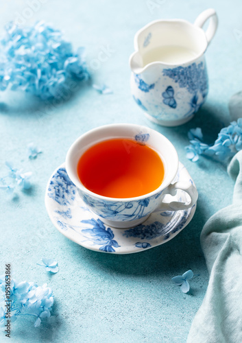 Refined tea presentation, blue floral porcelain, amber tea, hydrangea blooms. Calm blue background.